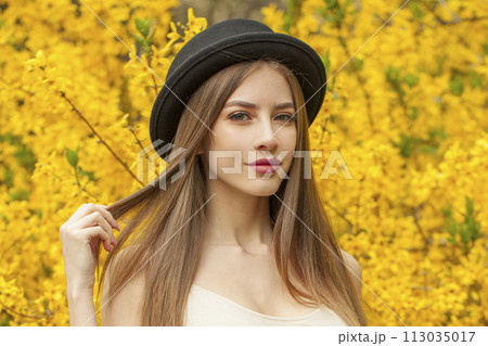 Smiling fashion model with long brown hair and natural makeup against floral background outdoor Smiling fashion model with long brown hair and natural makeup against floral background outdoor 113035017