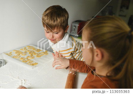 Brother and sister rolling out bunny cookie dough for Easter 113035363