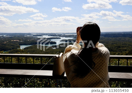 横山展望台の木もれ日テラスでスマホで写真撮影する女性 113035450