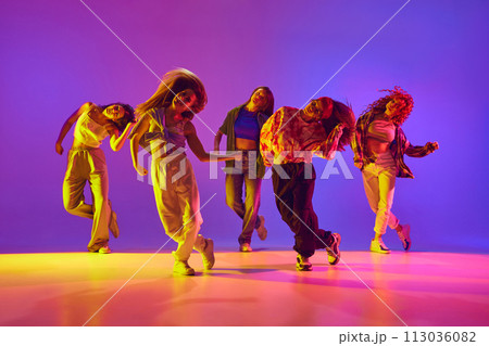 Dynamic image of young talented women in casual clothes in motion, dancing street style dance against gradient background in neon light 113036082