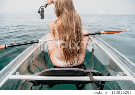 Woman in kayak back view. Happy young woman with long hair floating in transparent kayak on the crystal clear sea. Summer holiday vacation and cheerful female people relaxing having fun on the boat Woman in kayak back view. Happy young woman with long hair floating in transparent kayak on the crystal clear sea. Summer holiday vacation and cheerful female people relaxing having fun on the boat 113036295