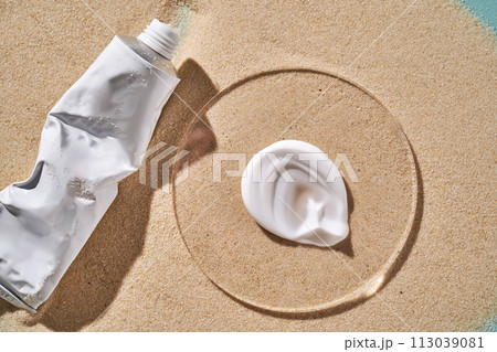 A tube of moisturizing sunscreen and a smear on a sandy background. 113039081