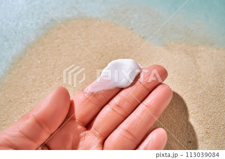 A smear of white cream with SPF on the fingers against a background of sand. 113039084