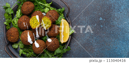 Plate of fried falafel balls served with fresh green cilantro and lemon top view on rustic concrete background. Traditional vegan dish of Middle Eastern cuisine, copy space 113040416