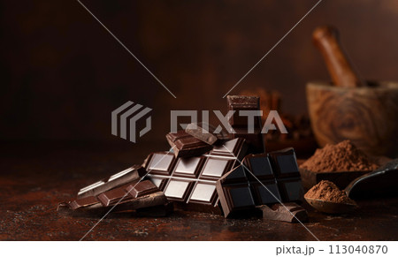 Broken dark chocolate bar and cocoa powder on a brown table. 113040870