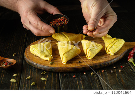 Cooking spring rolls with the hands of a chef on a kitchen board. Concept of cooking folded pancakes with filling and spices on kitchen table 113041664
