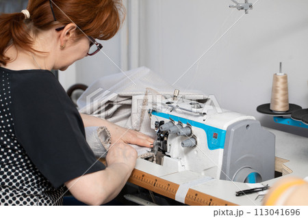 Experienced seamstress sews pillow covers on a sewing machine called overlock. 113041696
