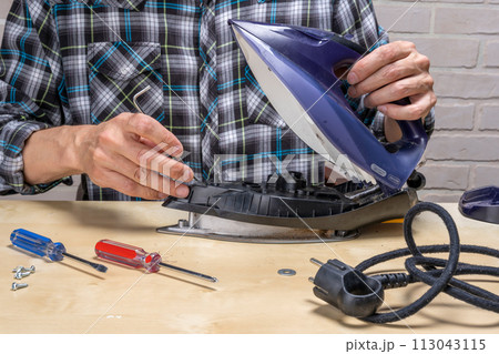 master repairs the iron in the workshop on the table using tools master repairs the iron in the workshop on the table using tools 113043115