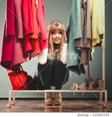 Scared woman hiding among clothes in mall wardrobe Scared woman hiding among clothes in mall wardrobe 113043316