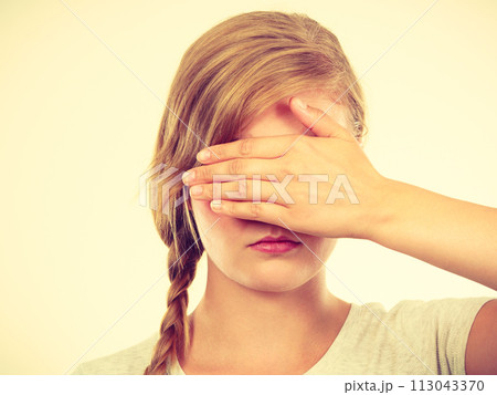 Shy teenage girl hiding face behind hand Shy teenage girl hiding face behind hand 113043370