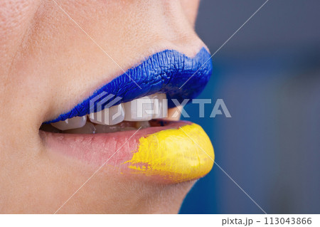 Close up of beautiful and plump female lips painted in blue and yellow. Lips of woman painted in Ukrainian flag colors. Close up of beautiful and plump female lips painted in blue and yellow. Lips of woman painted in Ukrainian flag colors. 113043866