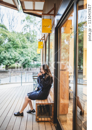 ベンチに座り飲み物を飲む女子高生 113043927