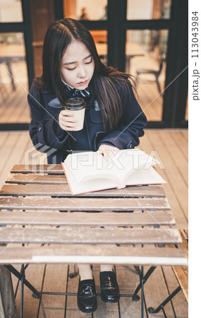 カフェの外の席で飲み物を飲みながら本を読む女子高生 カフェの外の席で飲み物を飲みながら本を読む女子高生 113043984