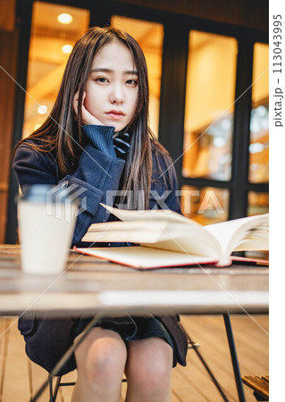 カフェの外の席で飲み物を飲みながら本を読む女子高生 カフェの外の席で飲み物を飲みながら本を読む女子高生 113043995