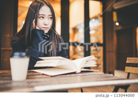 カフェの外の席で飲み物を飲みながら本を読む女子高生 カフェの外の席で飲み物を飲みながら本を読む女子高生 113044000