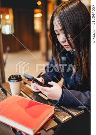 カフェで飲み物を飲みながらスマホをいじる女子高校生 カフェで飲み物を飲みながらスマホをいじる女子高校生 113044057