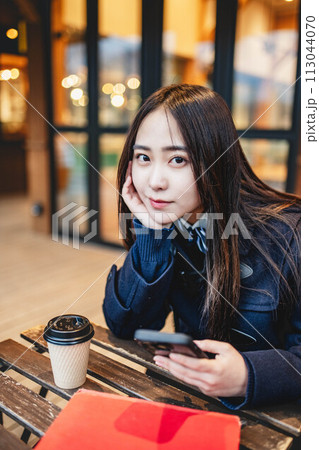 カフェで飲み物を飲みながらスマホをいじる女子高校生 カフェで飲み物を飲みながらスマホをいじる女子高校生 113044070