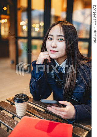 カフェで飲み物を飲みながらスマホをいじる女子高校生 113044072
