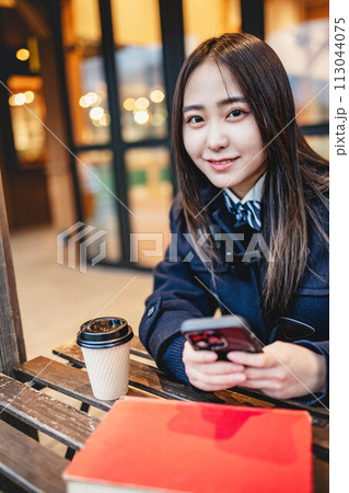 カフェで飲み物を飲みながらスマホをいじる女子高校生 113044075