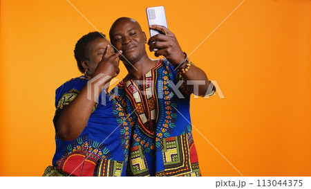 Happy african american couple capturing cute moment in studio, taking pictures on smartphone and enjoying leisure activity. Romantic married people take photos for memories on phone. Happy african american couple capturing cute moment in studio, taking pictures on smartphone and enjoying leisure activity. Romantic married people take photos for memories on phone. 113044375