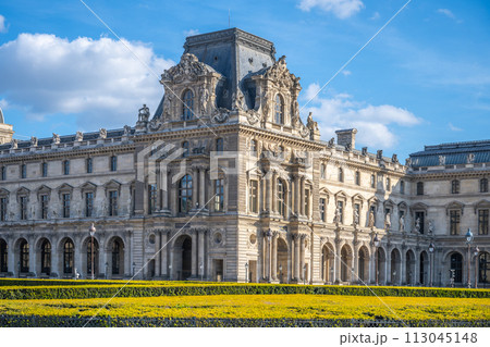 The majestic Louvre Museum basks in the sunlight against a clear blue sky, surrounded by manicured lawns. Paris, France 113045148