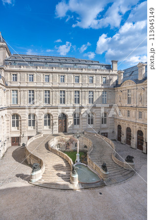 A double helix spiral staircase graces the cobblestone courtyard of the Louvre under a blue sky. Paris, France 113045149