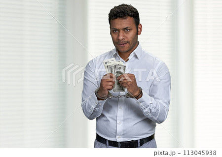 Young arrested man in handcuffs holding dollar banknotes. Businessman in handcuffs holding dollar bribe. 113045938