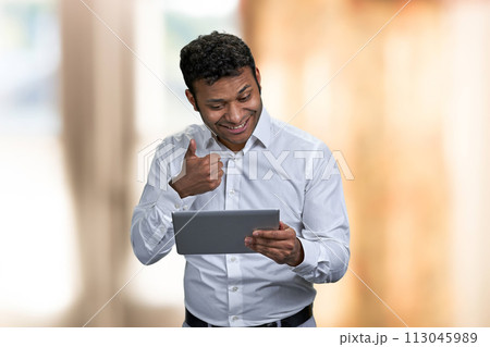 Handsome young businessman showing thumb up while having video call on digital tablet. Blur interior background. Handsome young businessman showing thumb up while having video call on digital tablet. Blur interior background. 113045989