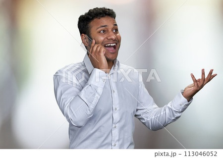Portrait of young excited business man using futuristic mobile phone. Happy surprised man in white shirt talking on glass phone on abstract bokeh background. 113046052