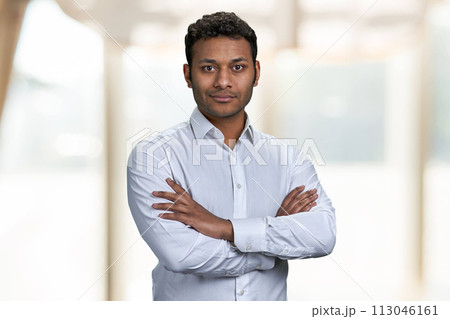 Attractive indian businessman looking at camera with crossed arms. Confident male executive standing on blur interior background. Attractive indian businessman looking at camera with crossed arms. Confident male executive standing on blur interior background. 113046161