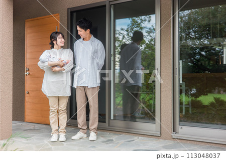 新築のマイホーム・一軒家・一戸建ての玄関の前に立つ施主の夫婦と赤ちゃん・カップル・家族 113048037