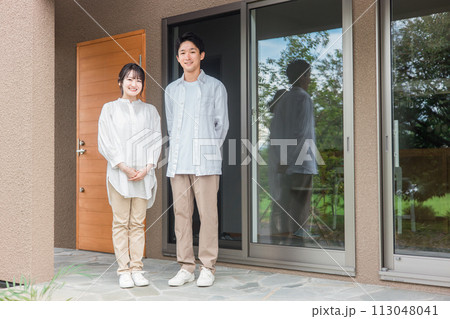 新築のマイホーム・一軒家・一戸建ての玄関の前に立つ施主の夫婦・カップル・家族 113048041