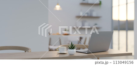A laptop on a wooden dining table in a contemporary minimalist white living room or dining room. A laptop on a wooden dining table in a contemporary minimalist white living room or dining room. 113049156