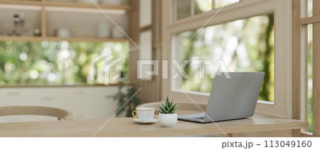 A laptop computer on a wooden dining table near by the window in a neutral contemporary kitchen. 113049160