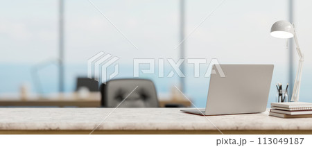 A back view image of a laptop computer on a white marble desk in a modern spacious office. 113049187