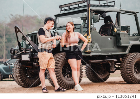 Cheerful couple shares a moment of laughter near a rugged off-road car, signaling a break in their adventurous journey. 113051241