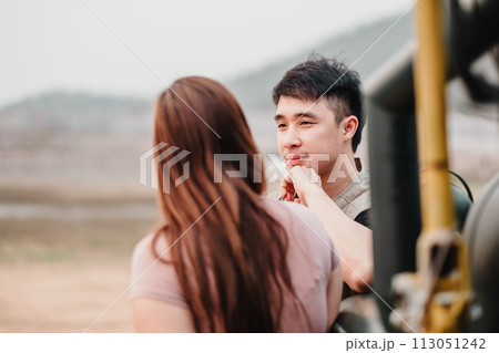 Tender scene as a woman gazes at a man, capturing an intimate, heartfelt exchange by their rugged car outdoors. Tender scene as a woman gazes at a man, capturing an intimate, heartfelt exchange by their rugged car outdoors. 113051242