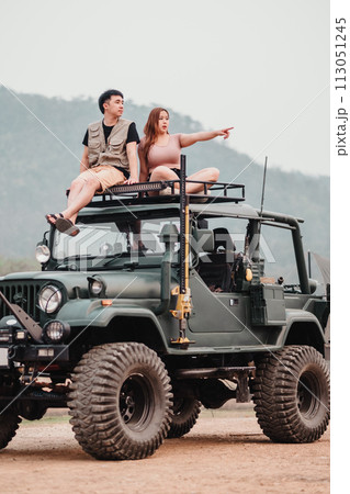 Adventurous couple is perched atop a rugged car, the woman pointing towards the horizon, ready for their next off-road exploration. Adventurous couple is perched atop a rugged car, the woman pointing towards the horizon, ready for their next off-road exploration. 113051245