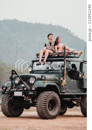 Adventurous couple is perched atop a rugged car, the woman pointing towards the horizon, ready for their next off-road exploration. 113051246