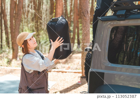 オートキャンプ場で車のルーフラックから荷物の積み下ろしをする男女・夫婦・カップル 113052387