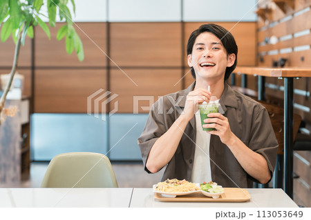 カフェでランチを食べながらグリーンスムージーを飲む若い男性（酵素・デトックス・食物繊維・健康食品） 113053649