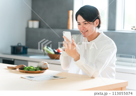 ダイニングで朝食を取りながらスマホを見る若いアジア人男性 113055074