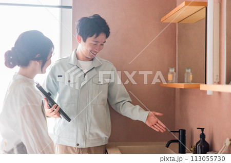 洗面所・洗面化粧台の水栓の説明をするハイスメーカーの男性と主婦の女性 113055730