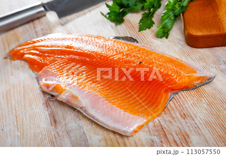 Trout fillet on cutting board with garlic and parsley Trout fillet on cutting board with garlic and parsley 113057550