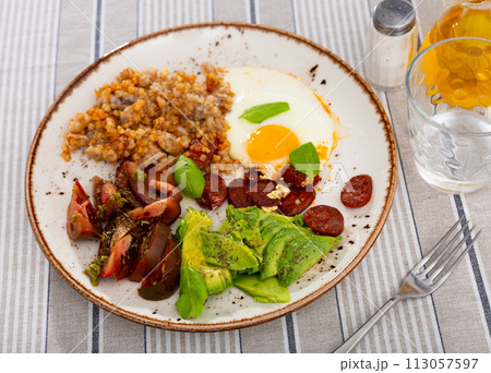 Homemade breakfast served with buckwheat, sun-dried tomatoes, avocado, fried eggs and hunting sausages 113057597