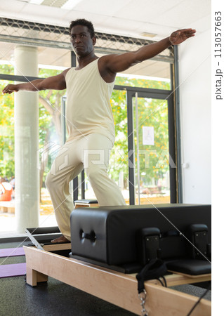 Concentrated African American man performing set of pilates exercises Concentrated African American man performing set of pilates exercises 113057663