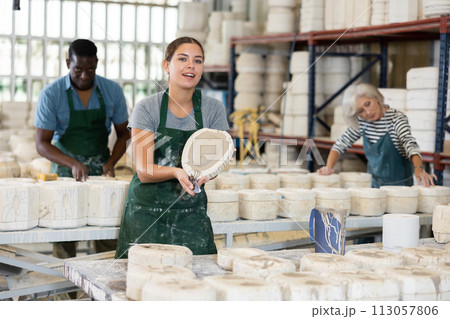Positive young worker demonstrates half of plaster mold for pottery in pottery factory 113057806