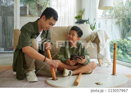 Smiling Vietnamese father and son assembling coffee table in living room Smiling Vietnamese father and son assembling coffee table in living room 113057967