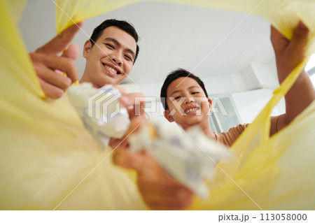 Smiling father and son sorting waste, view from plastic bag 113058000