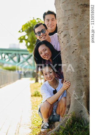 Smiling friends hiding behind tree when hanging out on river embankment 113058082